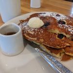 Stack of pancakes topped with cream and powdered sugar, served with syrup.
