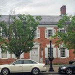 Historic red brick building with white trim, parked sedan in front on a cloudy day.