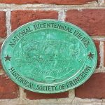 Green bronze plaque on red brick wall marking the National Bicentennial 1776-1976.