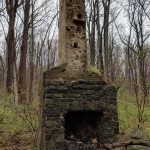 Ancient stone chimney structure amidst a dense, bare forest landscape.