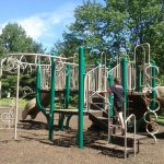 Child plays on a colorful playground structure with slides and climbing features outdoors.