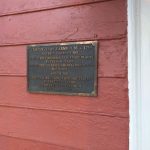 Historical marker on a red wooden building noting Temple-Ryan Farmhouse's listing.