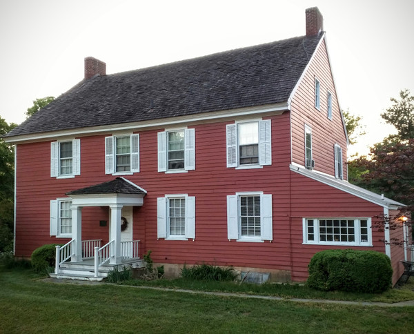 Red clapboard historic house with white trim and dark roof, set on a green lawn.