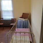 White crib in a bright room with window blinds and light yellow walls.