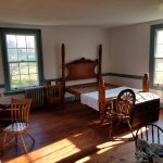 Rustic bedroom with a wooden bed, hardwood floors, and bright windows.