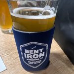 Craft beer in a branded pint glass featuring Bent Iron Brewing Co. logo on a navy sleeve.