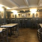 Rustic restaurant interior with wooden floors, dark walls, and marble-topped tables.