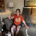 Woman in Sedona shirt sits on couch, holding a small object near framed Guinness ad.