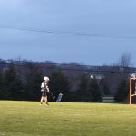 Football players on a grassy field under a cloudy sky during a game.
