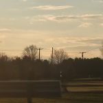 Sunset over a rural landscape with silhouetted trees and power lines against a cloudy sky.