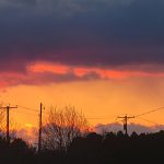 Dramatic sunset over silhouetted trees with vibrant orange and purple clouds.