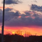 Vibrant sunset with dramatic clouds over a silhouetted landscape.