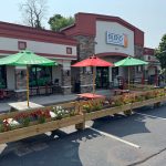 Outdoor dining area with green and red umbrellas in front of a modern commercial building.