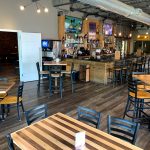 Rustic bar interior with wooden tables, stools, and a well-stocked bar area.