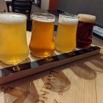 Four glasses of beer on a wooden serving board with "Gondavi 1966" visible.