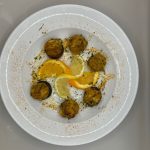 Fried balls and lemon slices on a white plate, sprinkled with herbs.