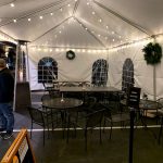 Tent dining area with tables and chairs under string lights, featuring arched windows.
