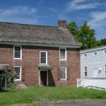 Historic brick house with white addition under a blue, cloudy sky.