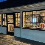 Exterior view of a shop with large windows and illuminated interior at dusk.