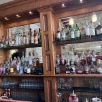 Wooden bar stocked with liquor bottles and glassware, featuring a stone backsplash.