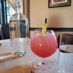Clear water bottle and pink cocktail on a wooden table indoors.