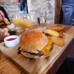 Gourmet burger on a wooden board with fries, set in a rustic indoor dining area.