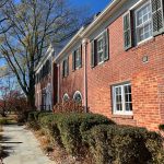 Red brick historic building with white trim and trees lining a stone walkway on a sunny day.