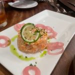 Salmon tartare topped with lime slices, served on a white rectangular plate.