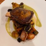 Seared pork chop served over roasted vegetables with a green sauce.