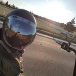 Motorcyclist in helmet on open road at sunset with a white fence lining the highway.