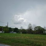 Overcast sky above a green field with scattered houses and trees.