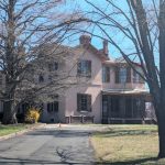 Historic pink house framed by large, bare trees on a sunny day.