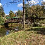 Wooden footbridge crosses a small stream in an autumn park setting.