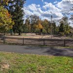 Autumn park playground with trees, black fence, and blue sky.