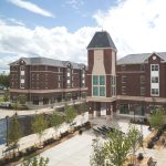 Modern brick university buildings under a partly cloudy blue sky.