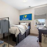 Blue and yellow Lions themed bedroom with a bed, desk, and gray curtains.