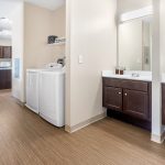 Laundry room with white washer and dryer next to a bathroom vanity mirror.