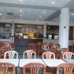Brightly lit, modern restaurant interior with dining tables and various food stall signs.