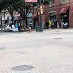 Street scene in a city with brick buildings, traffic light, and pedestrians on the sidewalk.