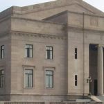 Neoclassical government building with large columns and stone facade under a bright sky.