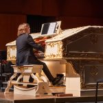 Musician plays a grand piano on stage during a performance.