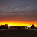 Sunset over a parking lot with a low-rise commercial building in the background.