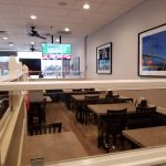 Interior view of a modern restaurant dining area with tables and a TV screen.