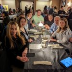Group of people gathered around a long table during an indoor event or meeting.
