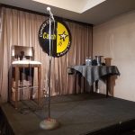Stage setup with a comedy club sign, microphone stand, and draped backdrop.