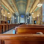 Interior view of a grand, high-ceilinged church nave with wooden pews and stained glass.