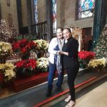 Two women pose inside a grand church with festive holiday decorations.