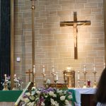 Christian church interior with a crucifix, stone walls, and floral arrangements.