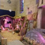 Nativity scene display with figures, straw ground, and architectural backdrop.