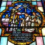 Stained glass panel depicting a religious scene with figures gathered around a central symbol.